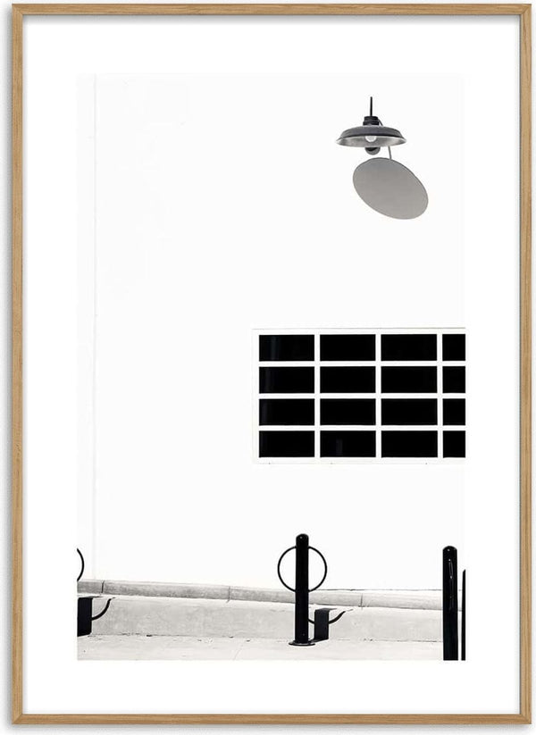 Black lamp on a white wall with grid window and minimal street elements, featured on a poster.