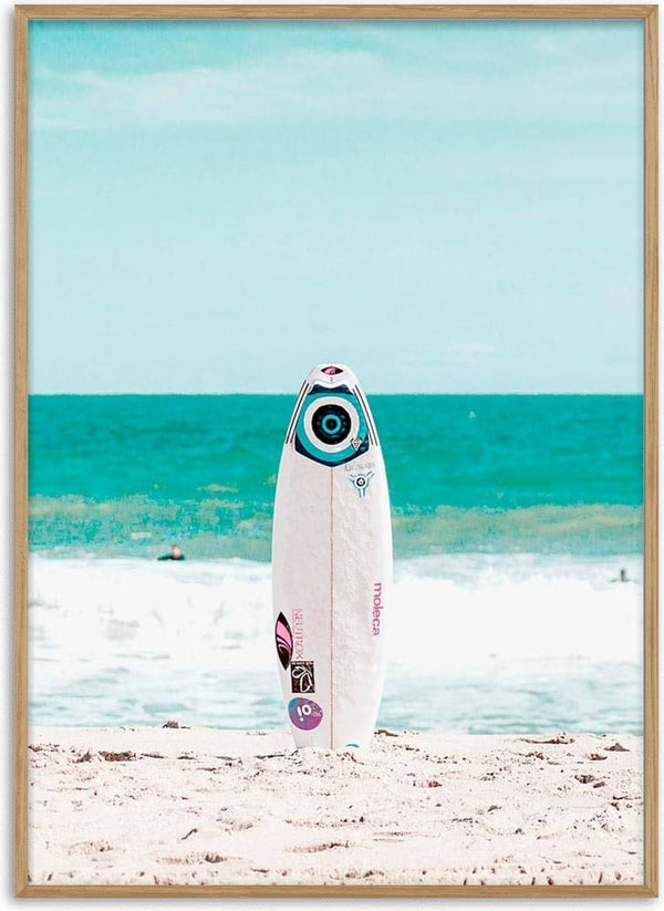 White surfboard standing upright on sandy beach with blue ocean waves in the background.