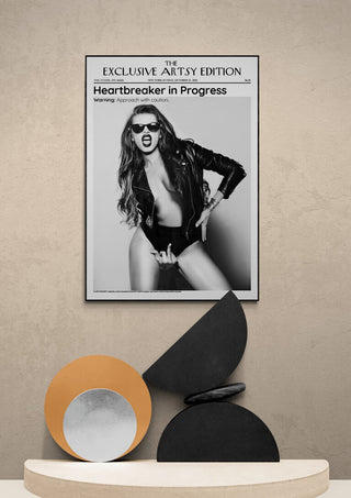 Framed "Heartbreaker in Progress Artsy Edition" poster above modern decorative sculpture on a beige wall.