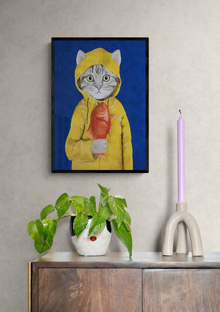 Framed Cat With Fish - Coco de Paris artwork above a cabinet with a potted plant and pastel candle.